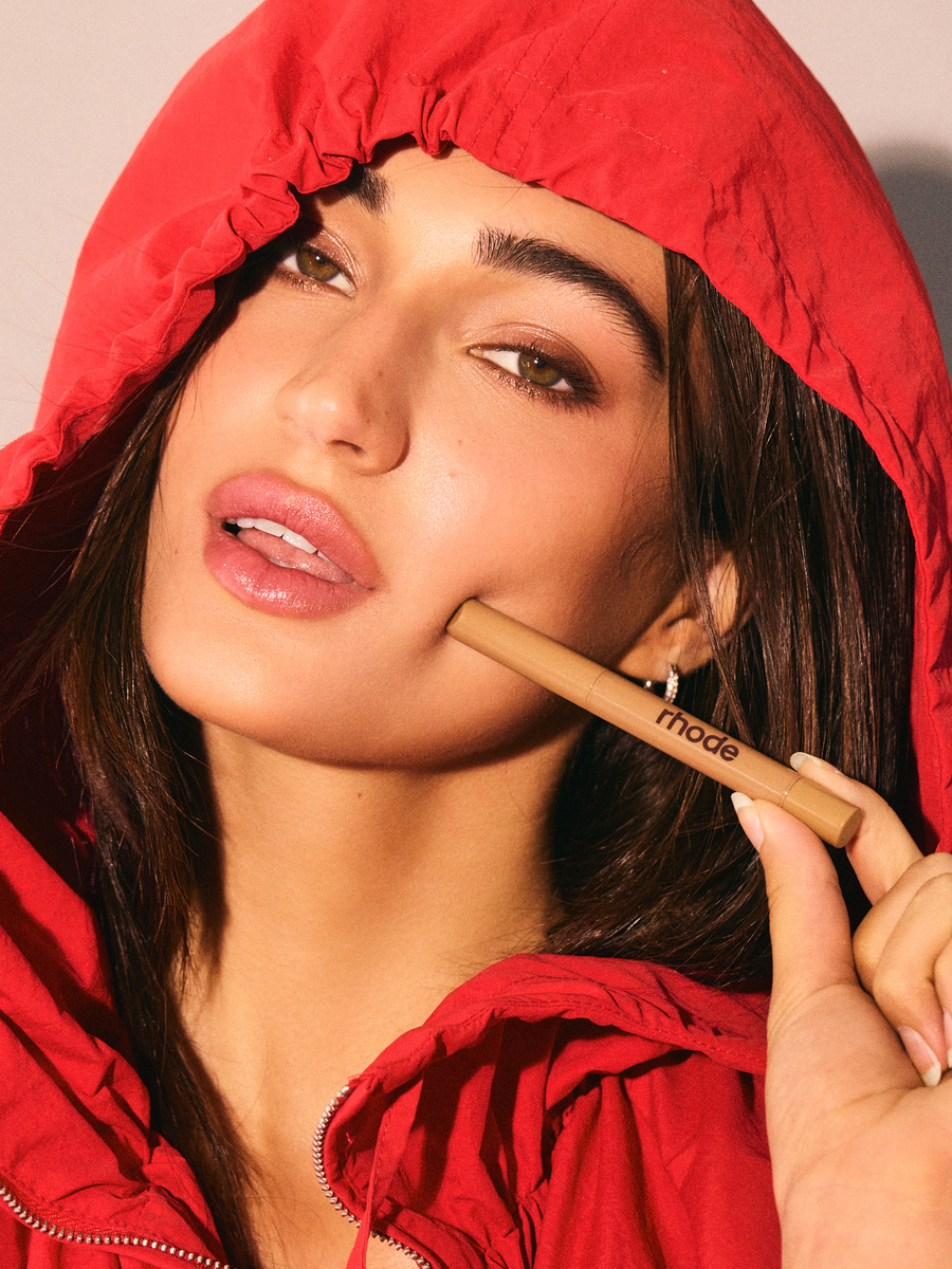 Model Rachel Carillo in a red hood holding a Rhode beauty product during a cosmetics spec shoot at Know Good Studio in Miami.